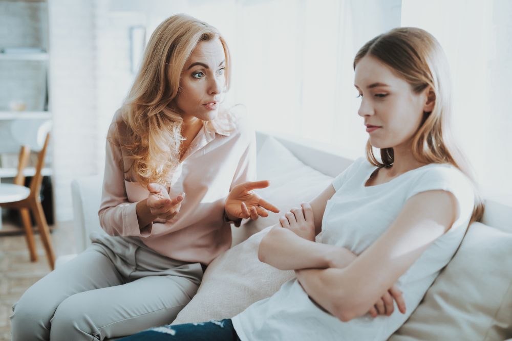 mom talking to teenage daughter on couch, both looking tense